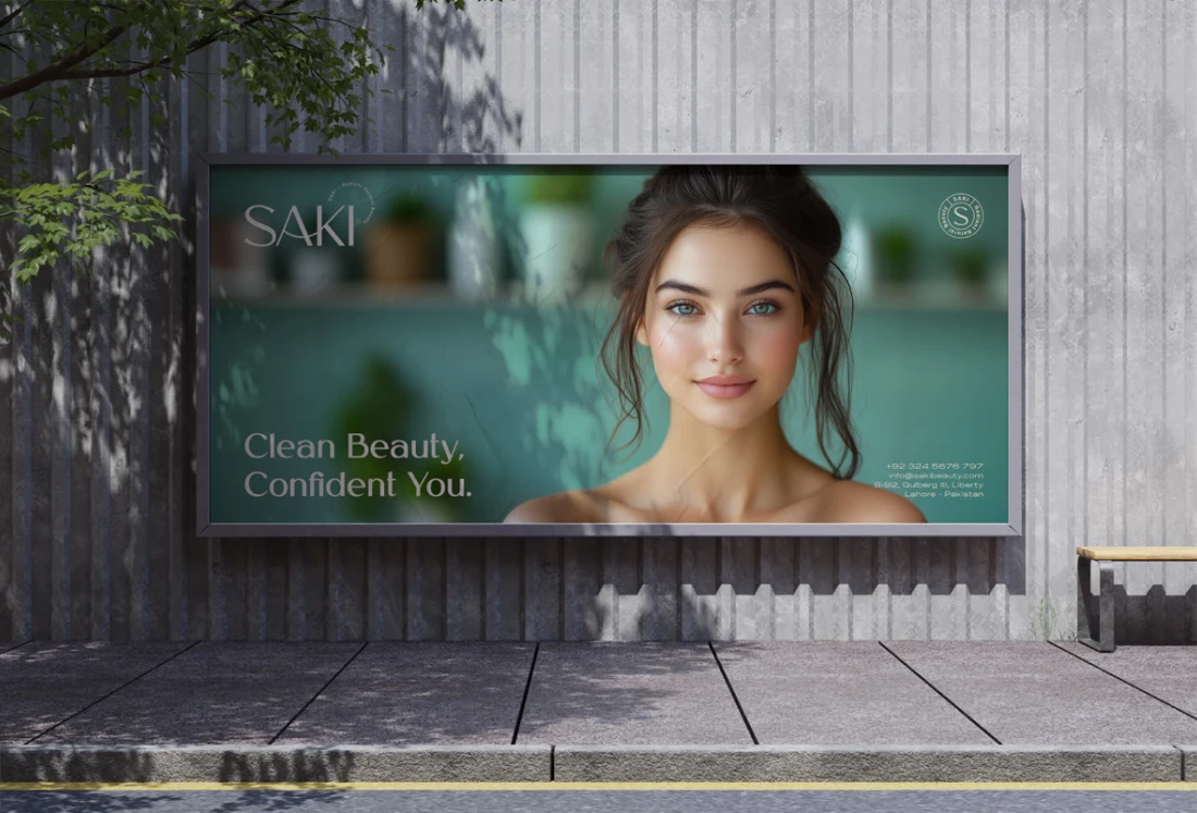SAKI clean-beauty billboard beside a concrete wall and greenery.